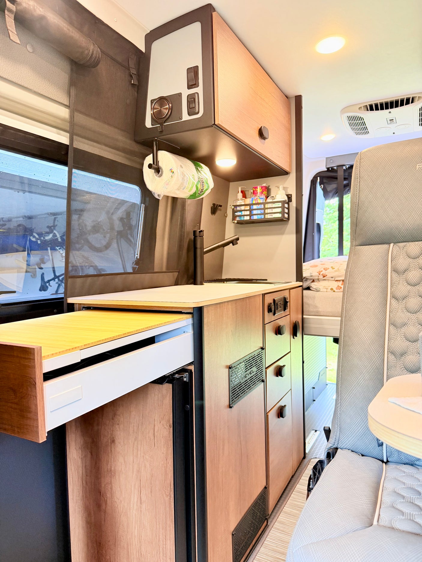 Cozy RV rental kitchen area in a Winnebago Revel camper van, featuring a sink, pull-out counter, and storage.