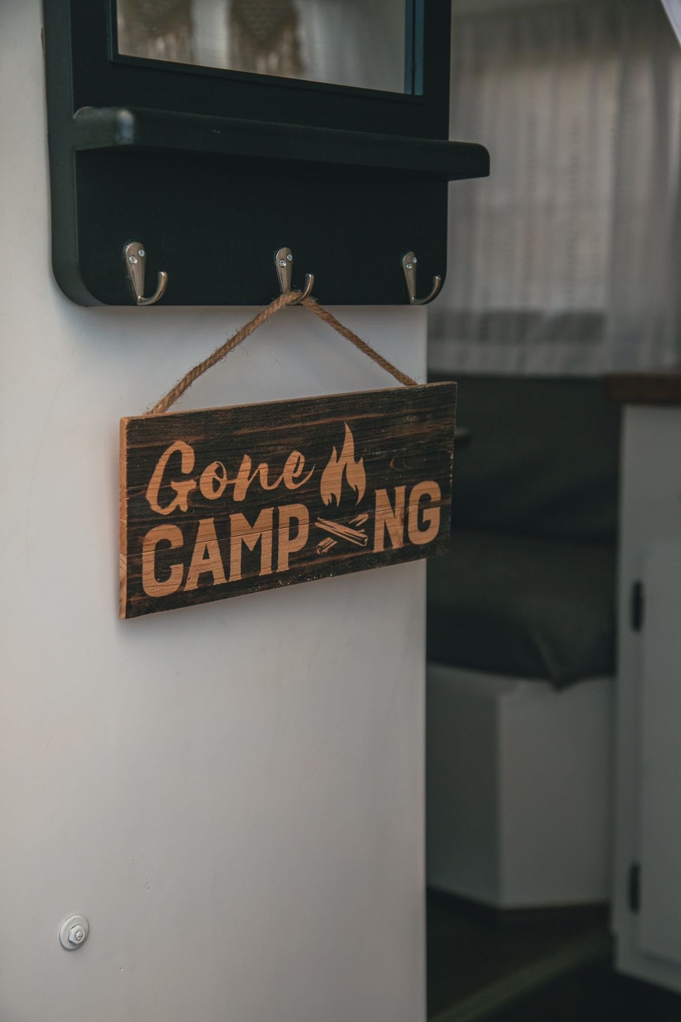 A 'Gone CAMPING' wooden sign, featuring a campfire icon, hangs from a dark shelf inside an RV rental.