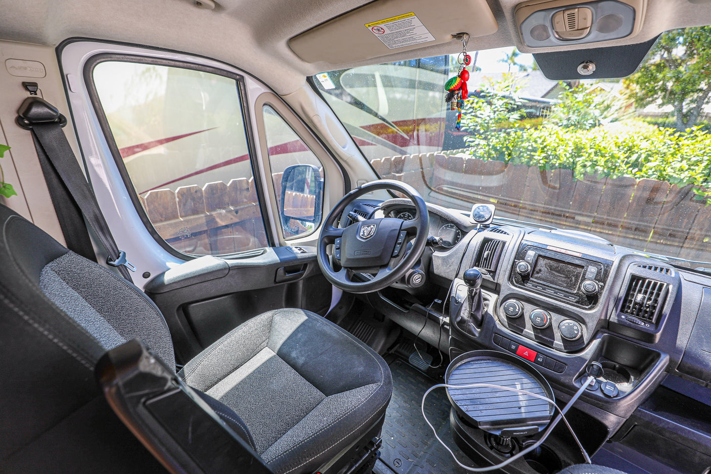 Inside a spacious RV rental van, featuring the driver's seat, dashboard, and steering wheel. Views of another RV outside.