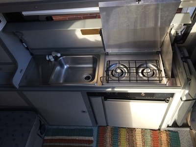 snow-dusted RV rental parked by a snowy lake with mountain views.|Inside an **rv rental**: a compact kitchen with a stainless steel sink