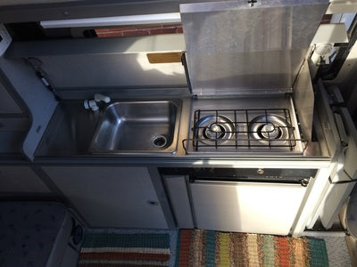 snow-dusted RV rental parked by a snowy lake with mountain views.|Inside an **rv rental**: a compact kitchen with a stainless steel sink