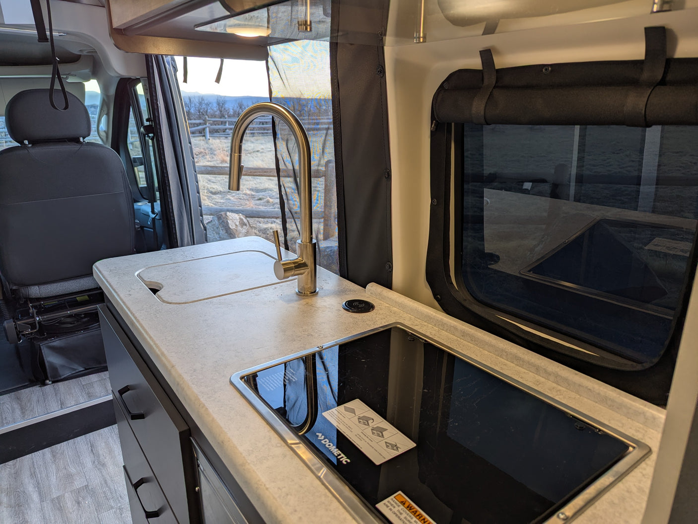 Modern RV rental interior: A compact kitchen with sink, induction cooktop, and charging pad, next to the passenger seat.