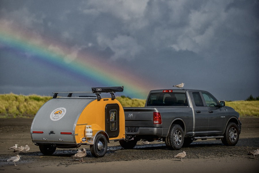 Experience outdoor adventure! This RV rental teardrop trailer towed by a truck under a rainbow offers perfect camping trips.