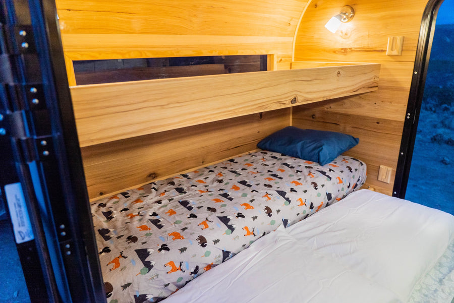 Cozy wooden RV rental interior with bunk beds. The lower bed features a forest animal sheet & blue pillow.