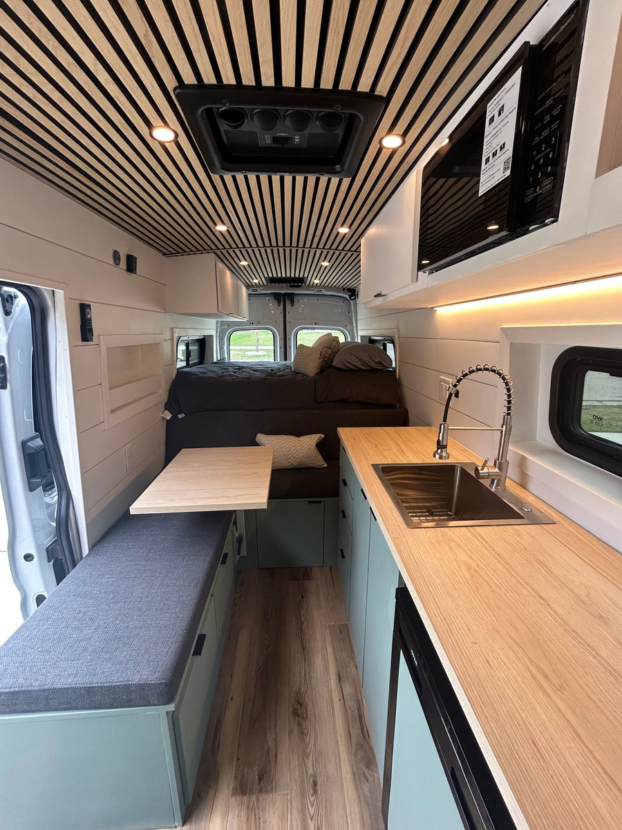 Modern rv rental interior with a sleek slat wood ceiling, full kitchen, dining bench, and cozy bed area.