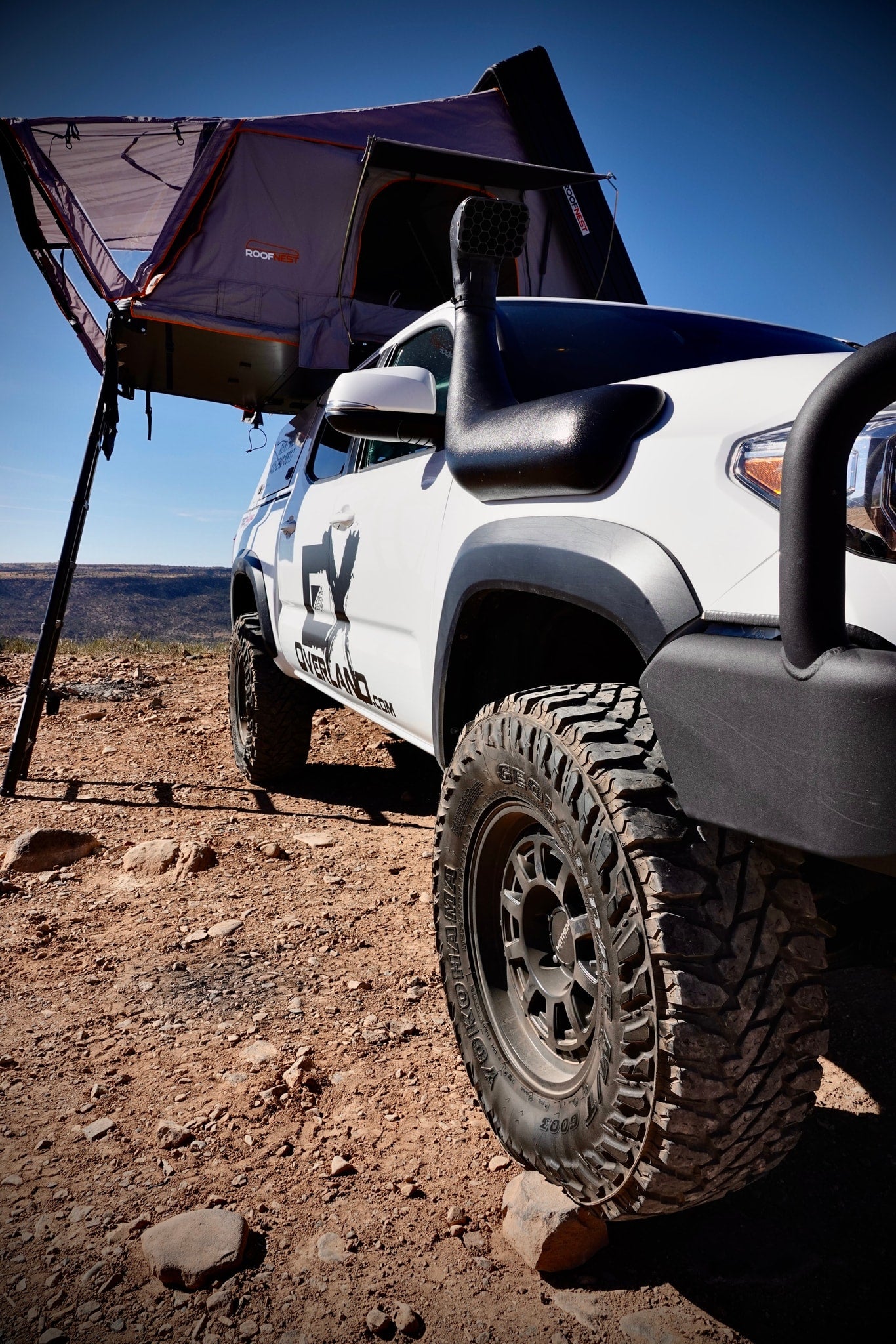 White overland vehicle with a Roofnest roof-top tent deployed on rocky terrain. Ideal for an RV rental off-road camping trip.