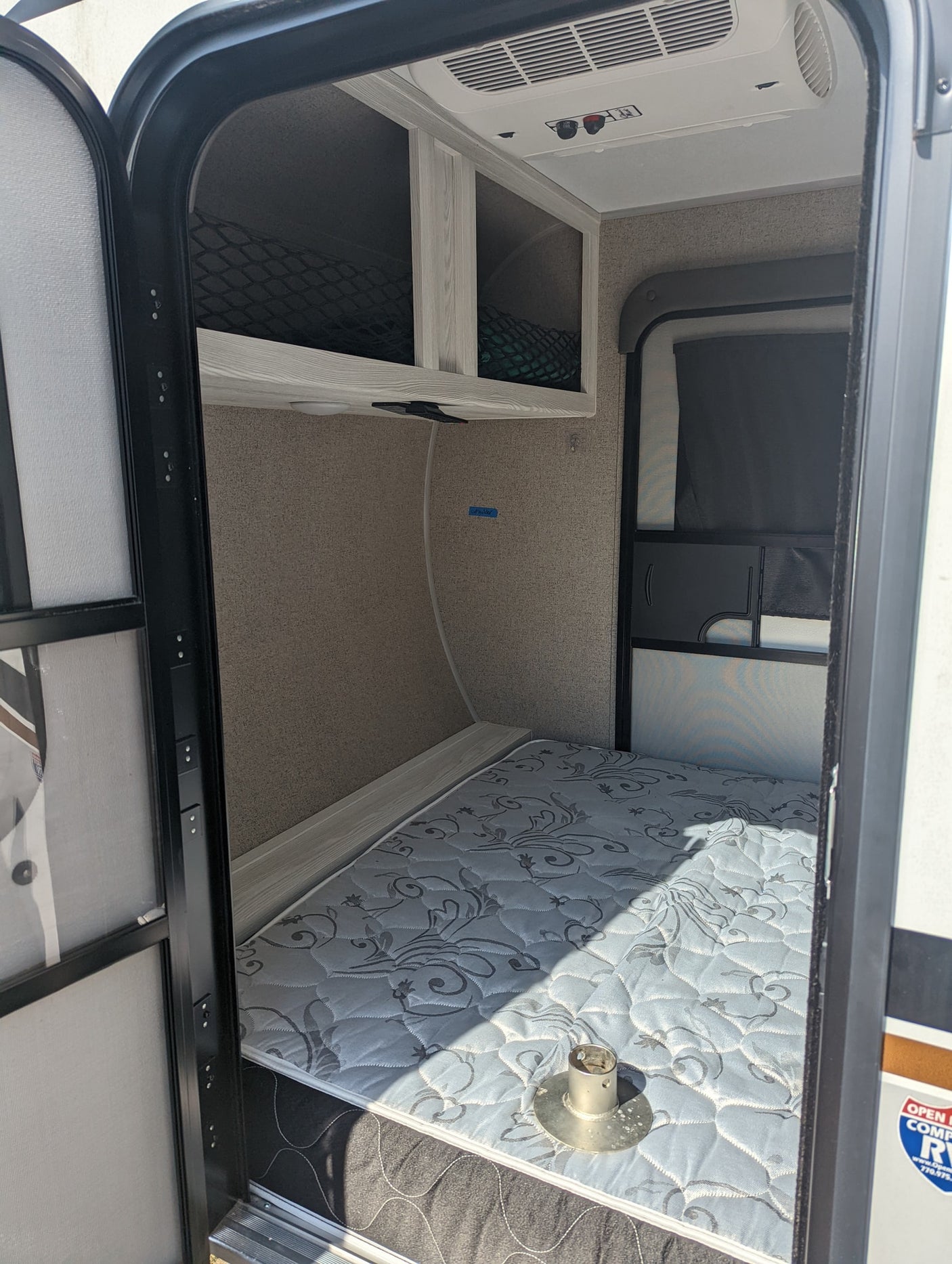Step into this RV rental, featuring a lower bunk bed with mattress, upper storage cubbies, and overhead AC unit.