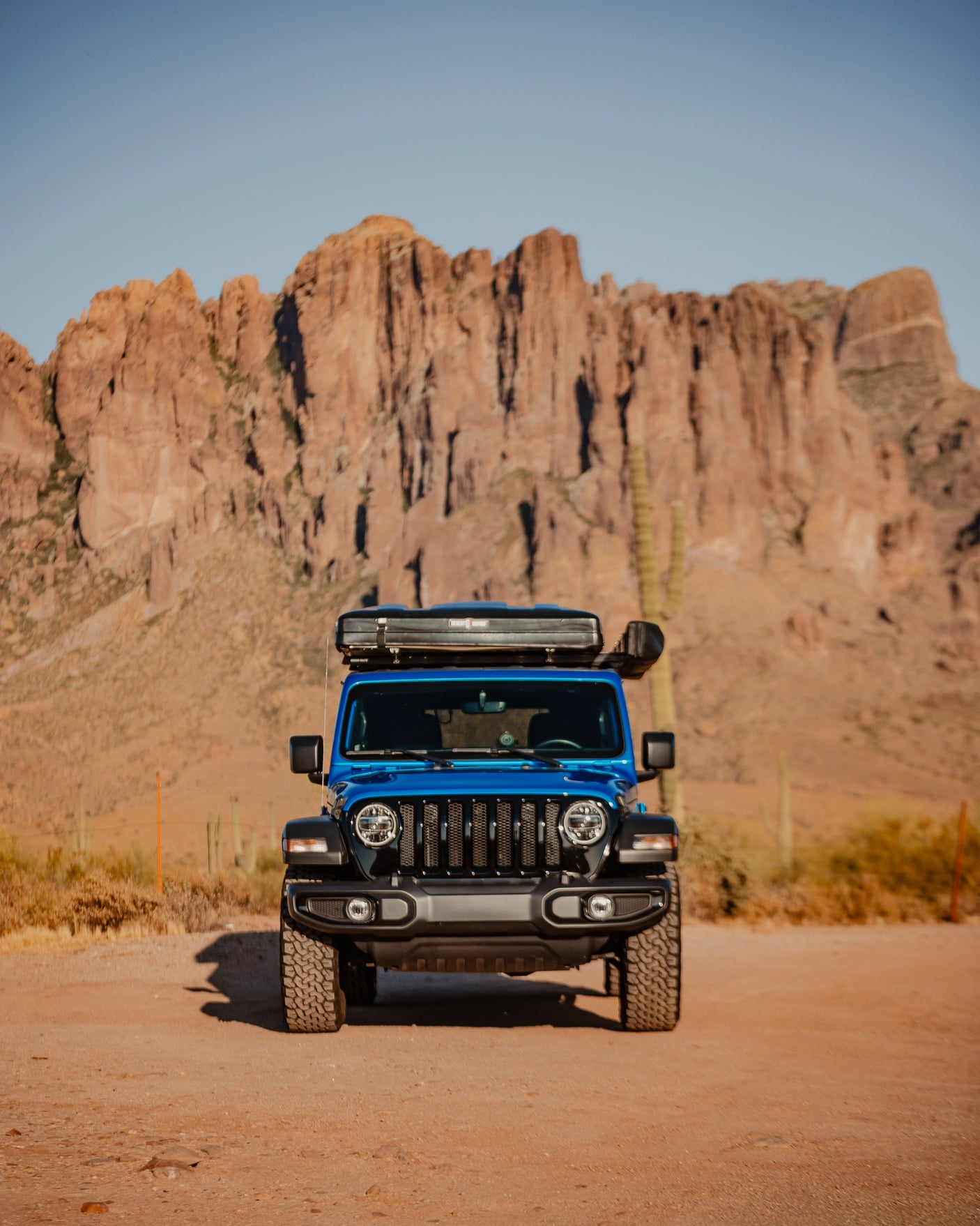 A blue Jeep with a rooftop tent is parked on a dirt road, ready for adventure. Explore desert mountains; a unique RV rental alternative for off-road camping.