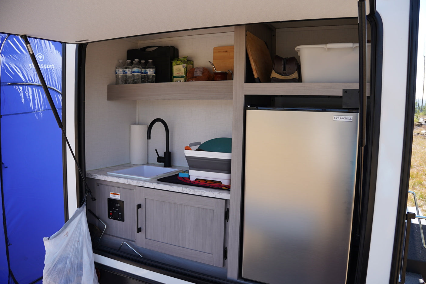 Outdoor RV rental kitchen with sink, Everchill mini-fridge, and shelved storage for easy outdoor cooking.