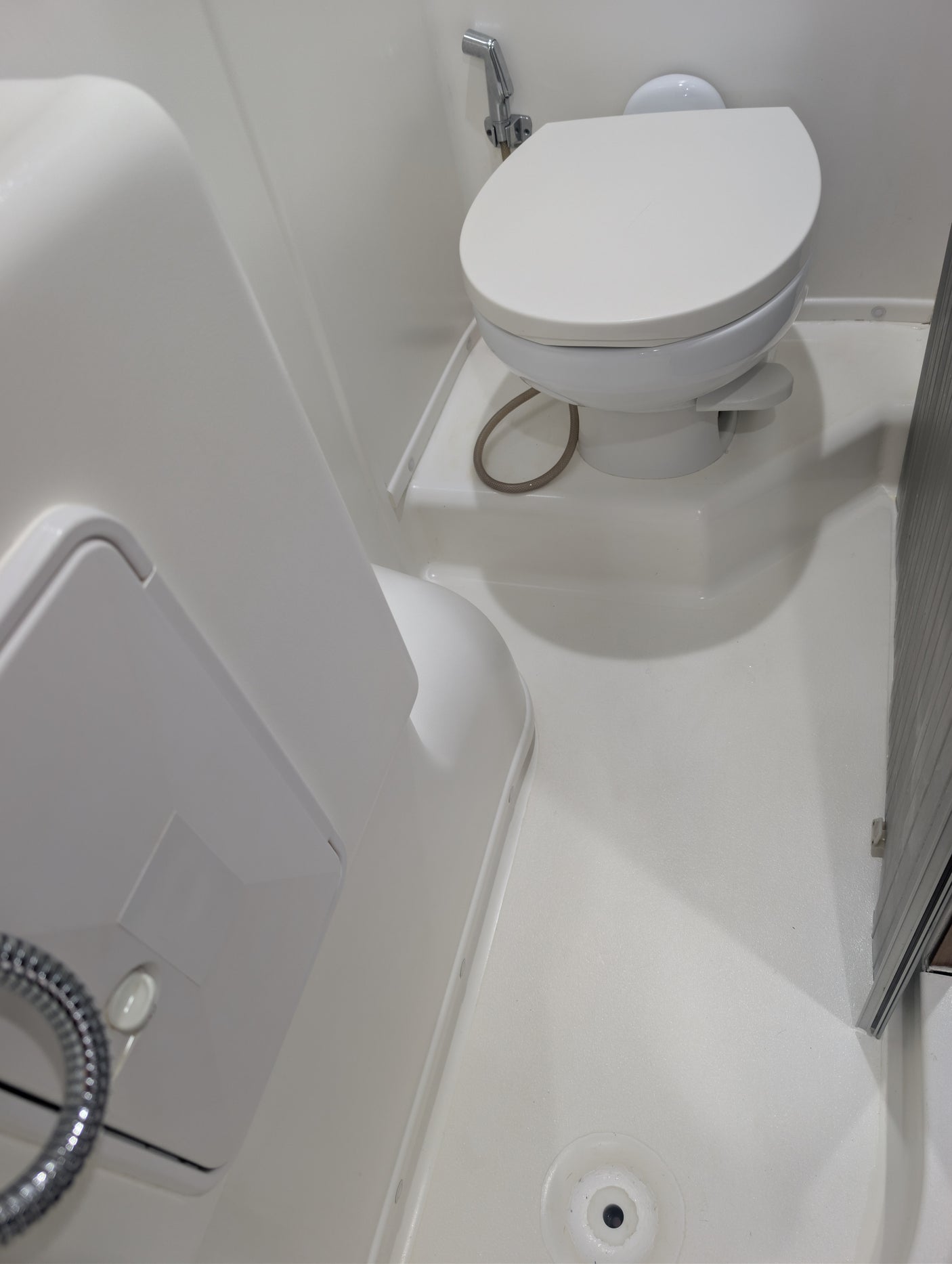 RV rental: Compact, all-white bathroom with a toilet, bidet sprayer, shower hose, and floor drain, optimizing space for travel.