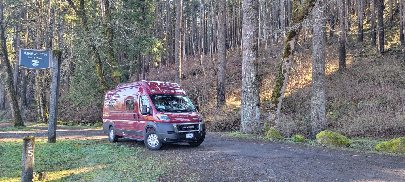 A red RV rental, a Ram ProMaster camper van, sits by campsite 35 in Ainsworth State Park, Oregon.
