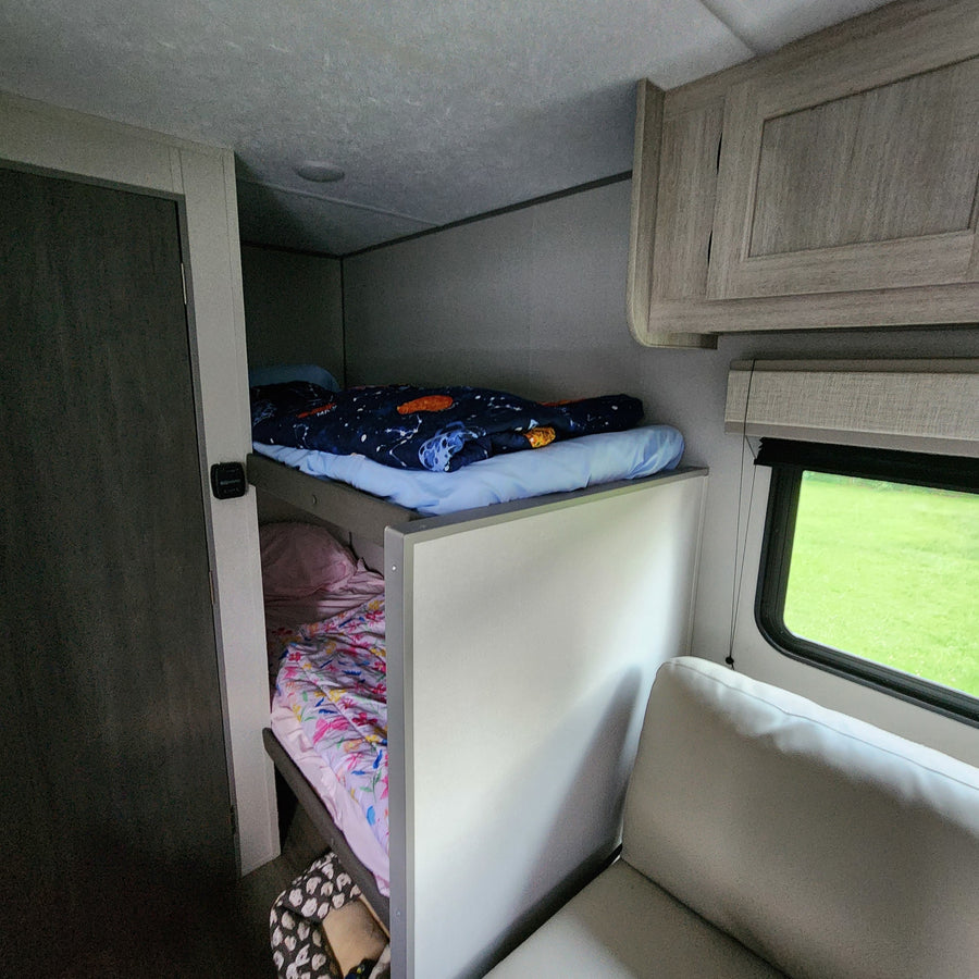 Inside an rv rental: comfortable bunk beds with colorful bedding and an exterior view from the window.