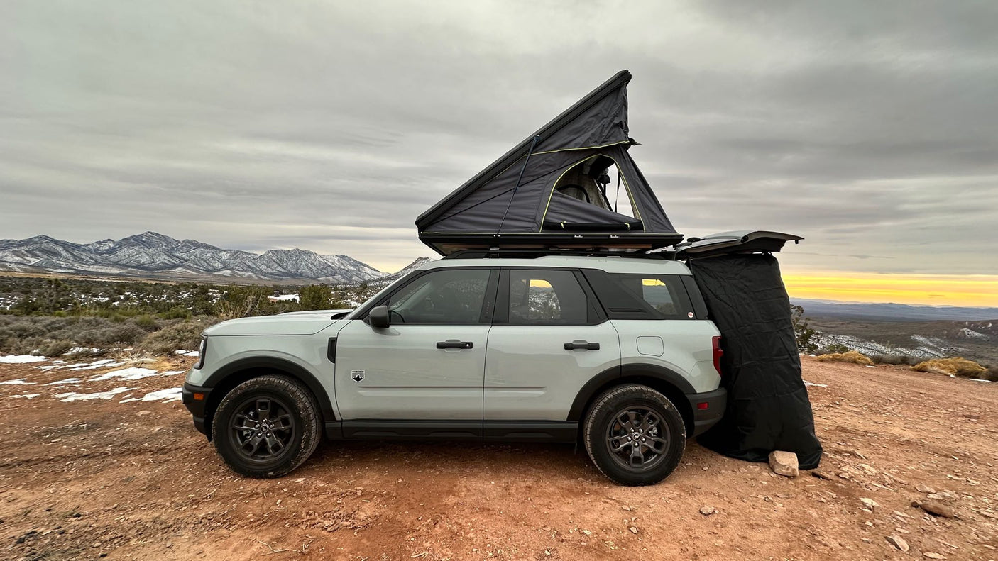 Light grey Ford Bronco Sport SUV with a rooftop tent and rear privacy room. Set up in snowy mountain terrain
