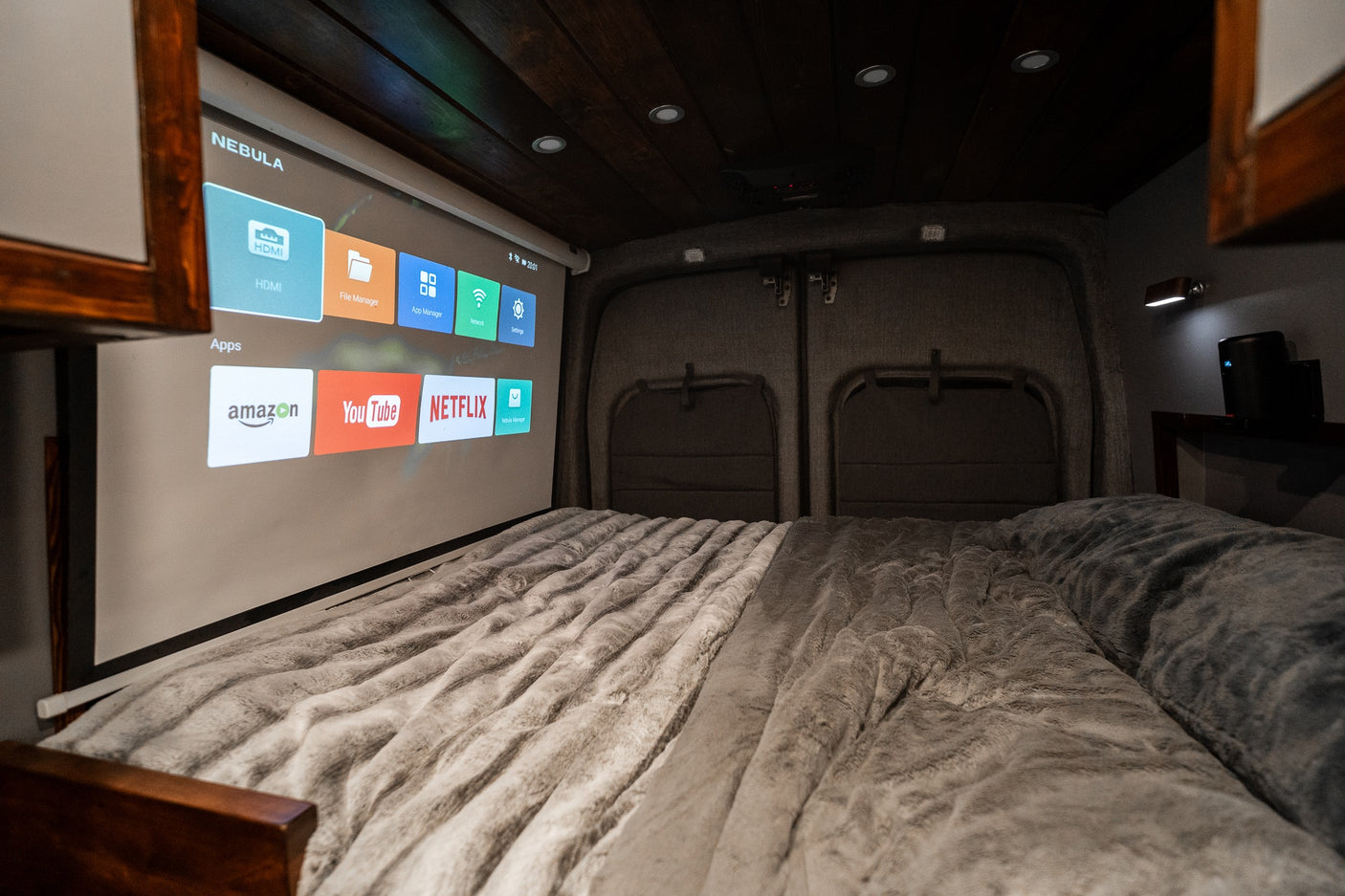 Cozy RV rental interior with a large projector screen displaying Netflix, YouTube, and Amazon over a plush bed.