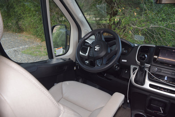 Inside an rv rental, featuring the cockpit with a Ram steering wheel, dashboard, gear shift, and serene natural view.