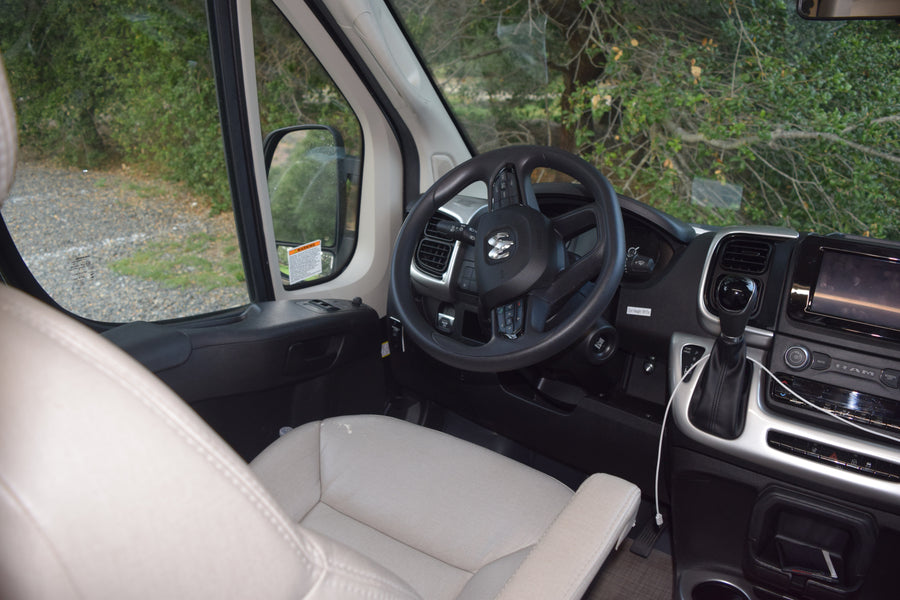 Inside an rv rental, featuring the cockpit with a Ram steering wheel, dashboard, gear shift, and serene natural view.