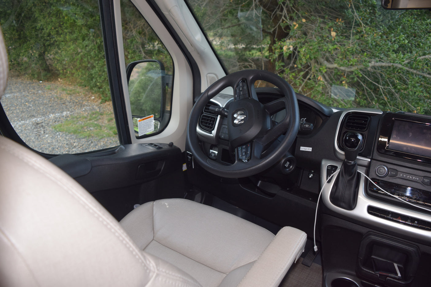 Inside an rv rental, featuring the cockpit with a Ram steering wheel, dashboard, gear shift, and serene natural view.
