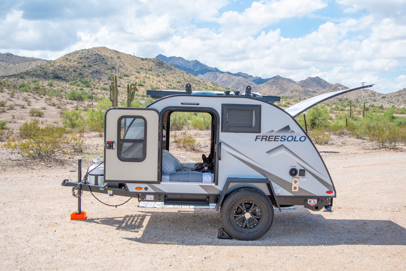 This RV rental teardrop camper is set up in a scenic desert landscape, perfect for outdoor adventure with a dog inside.