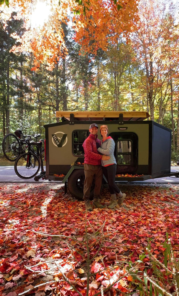 and a large convertible table/bed platform.|An RV rental: a dark green travel trailer with its back hatch open to reveal a kitchen. An awning extends
