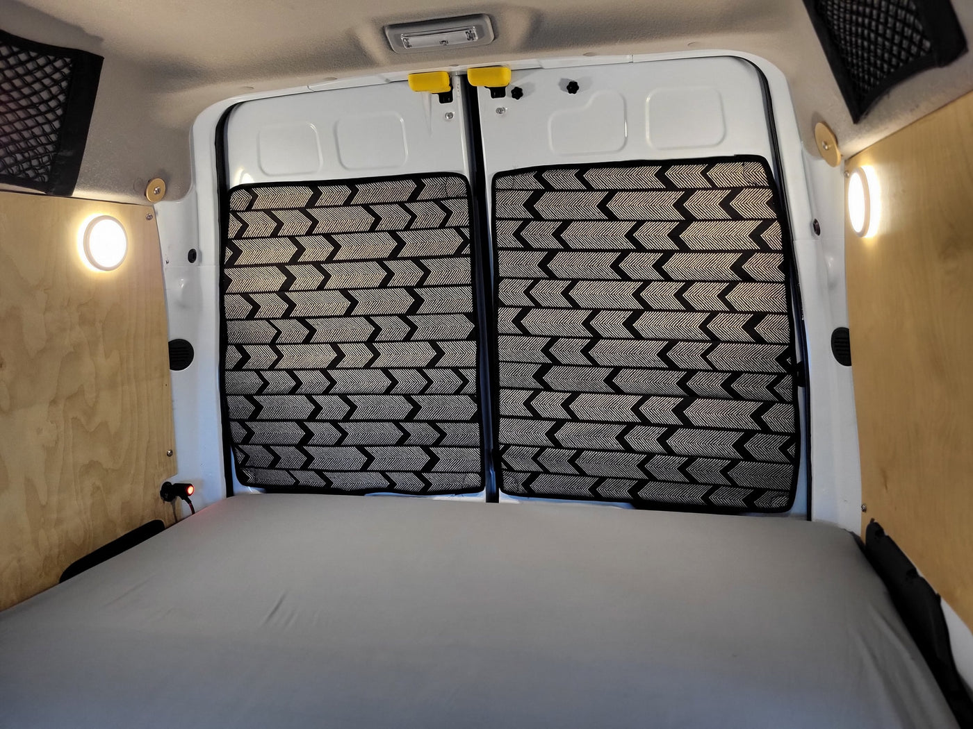 with a rainy view outside.|This RV rental features a cozy sleeping area: a grey mattress on a wooden slat bed — photo 12