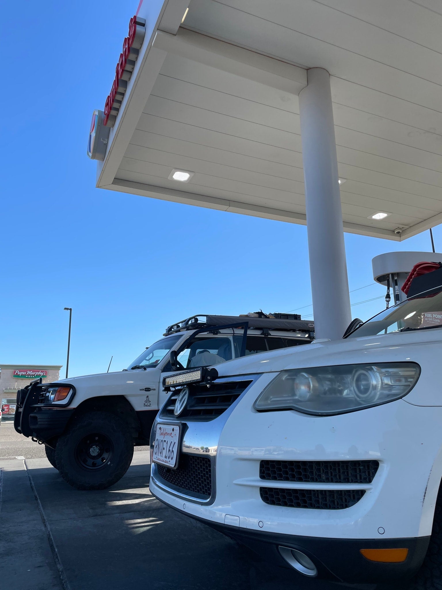 Two white adventure vehicles, an off-road SUV & VW Touareg, refueling at a station, perfect for an RV rental trip.