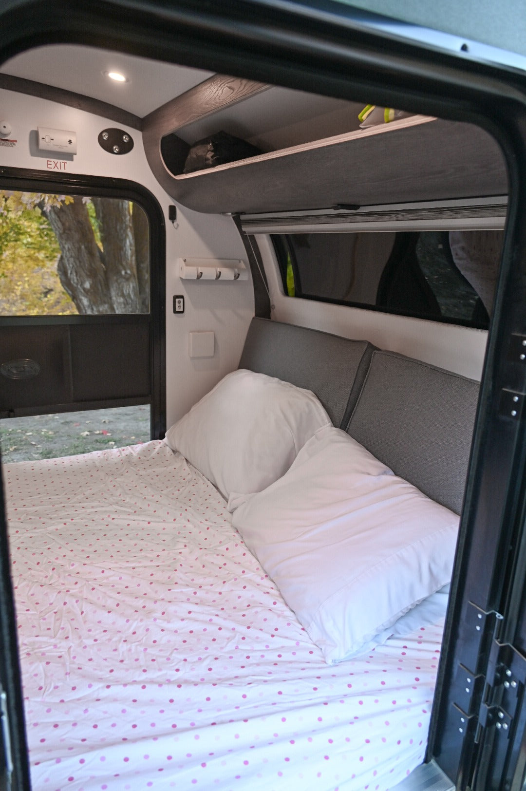 RV rental interior: A cozy bed with pink polka-dot sheets, white pillows, and overhead storage awaits adventurers.