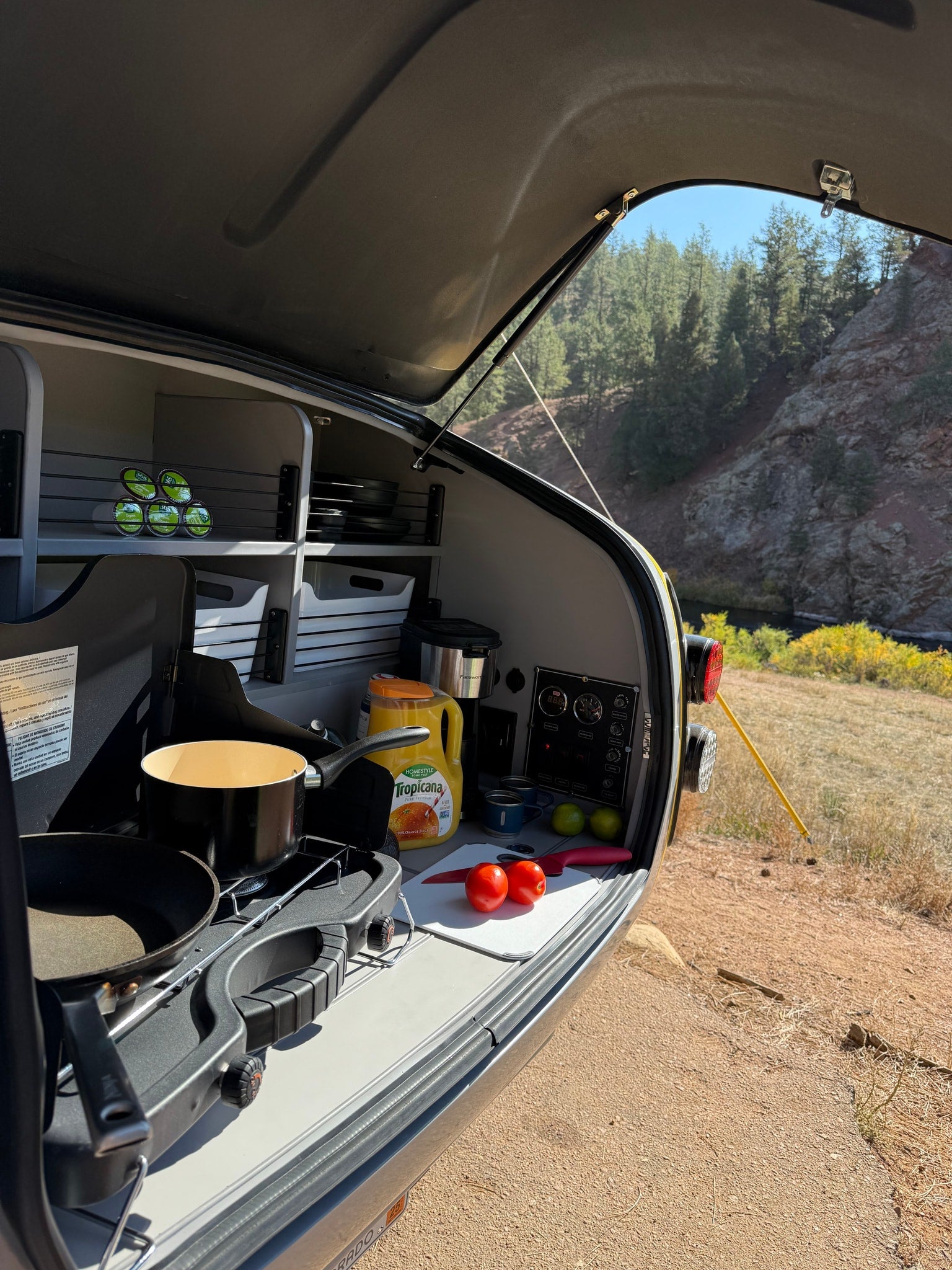 Teardrop RV rental: Outdoor kitchen with stove, food prep, and storage ready for cooking by a scenic river.