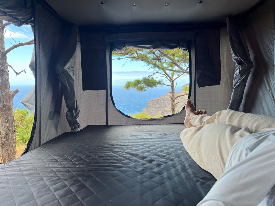 Relaxing in an RV rental's cozy rooftop tent, offering stunning ocean and cliff views. A perfect nature escape.