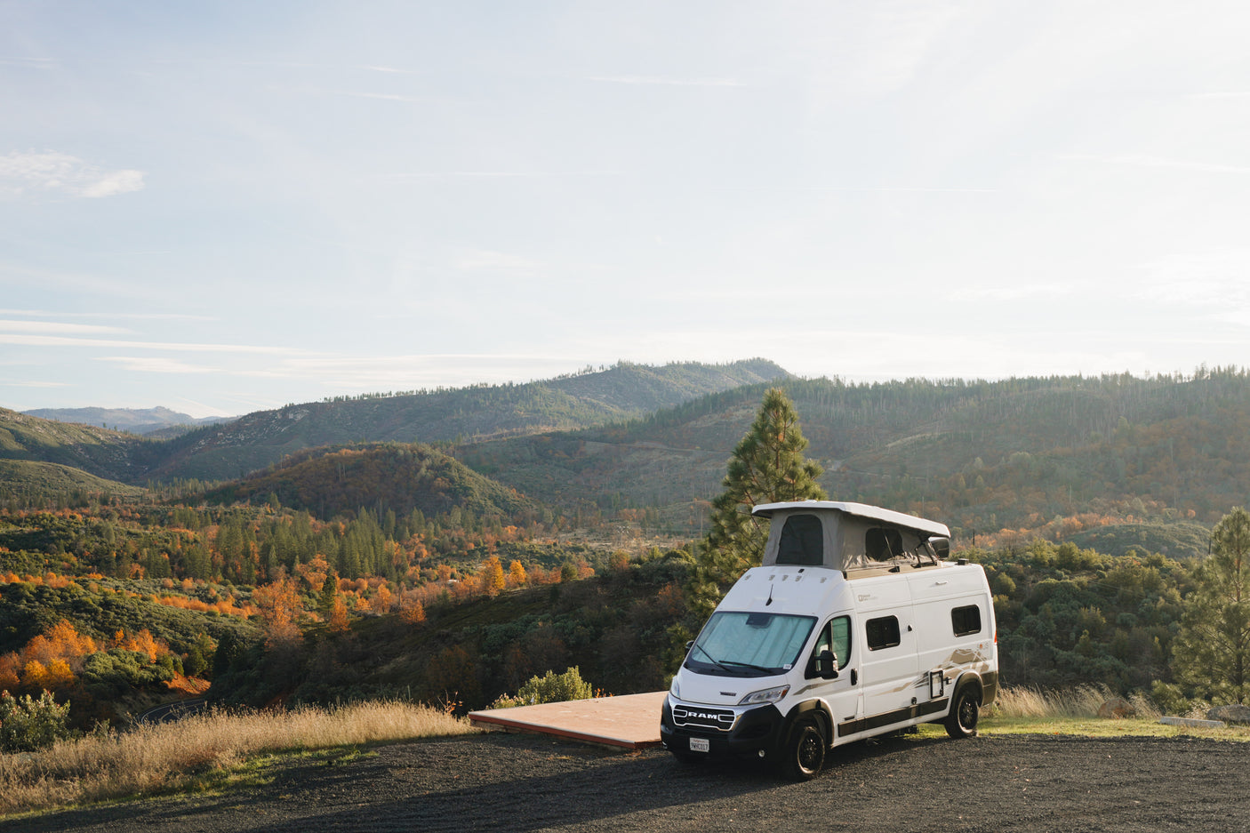 White RV rental camper van with a pop-top, parked at a scenic overlook, surrounded by vibrant autumn mountains.