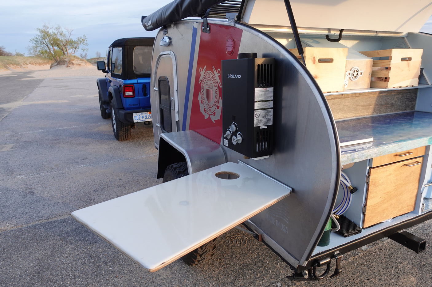 An rv rental teardrop trailer with a Coast Guard theme and an outdoor kitchen, ready for adventure with a Jeep.