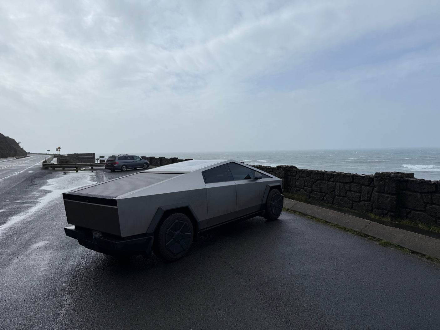 Sleek Tesla Cybertruck on a wet coastal road overlooking a stormy ocean. Forget an RV rental, this is modern exploration.