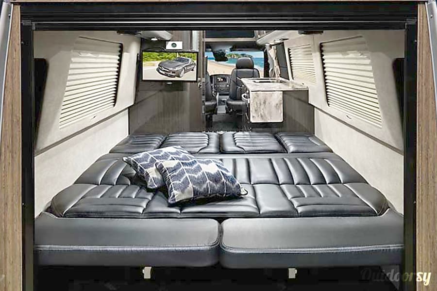 featuring patterned pillows and bright windows for a comfortable journey.|Cozy RV rental interior: black leather seating