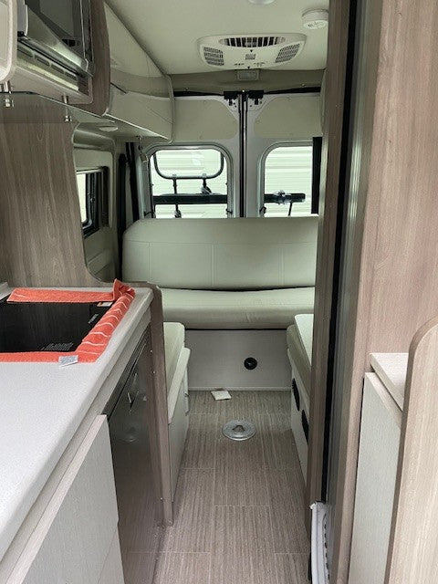 Explore this clean RV rental interior, showcasing a bright kitchenette, rear lounge/bed, and wood-look flooring. Ready for adventure!