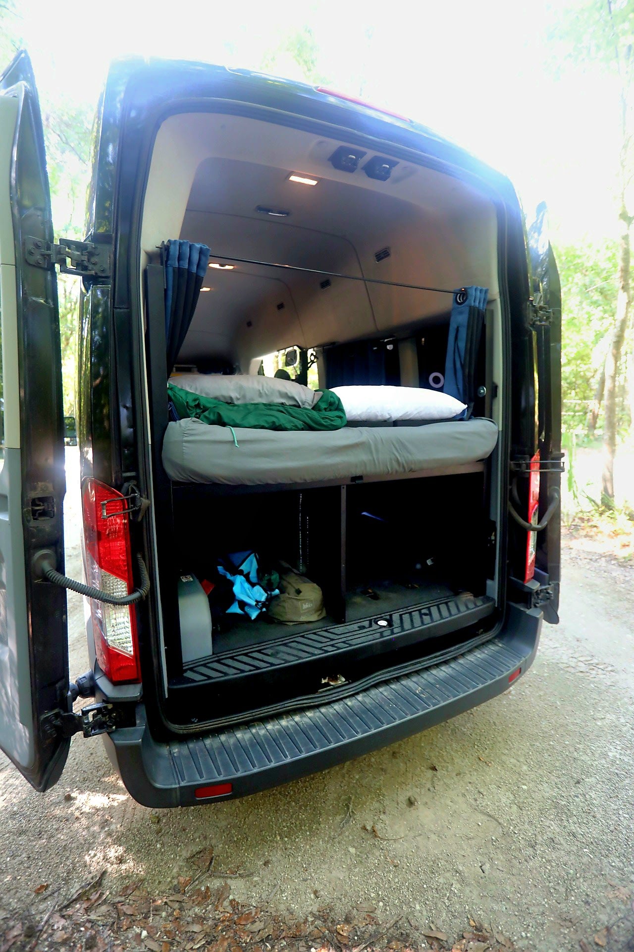 next to a cozy bed. Blue curtains complete the look.|Black Ford Transit WANDERVANS camper van