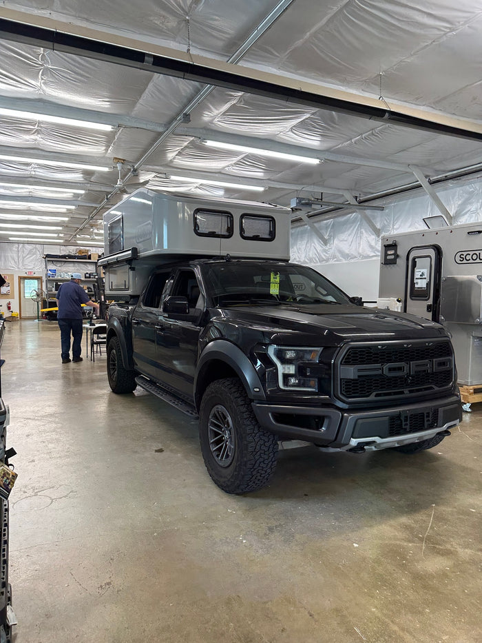 A black Ford Raptor with a Scout truck camper, adventure-ready for your next RV rental journey.