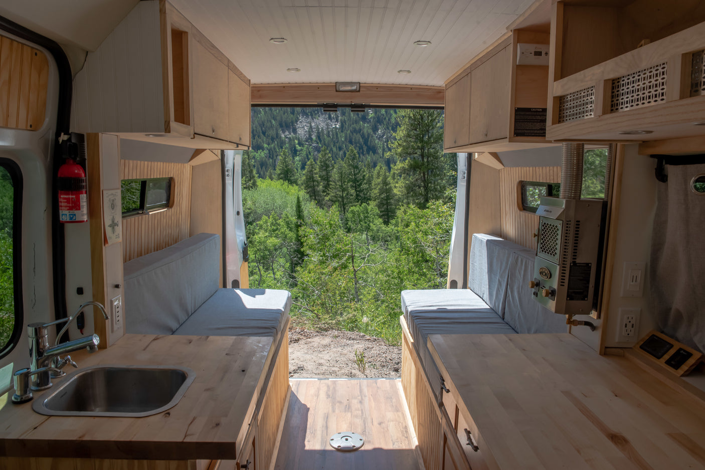 RV rental interior: a clean camper van with kitchen, benches, and an open back showcasing a stunning forest view.