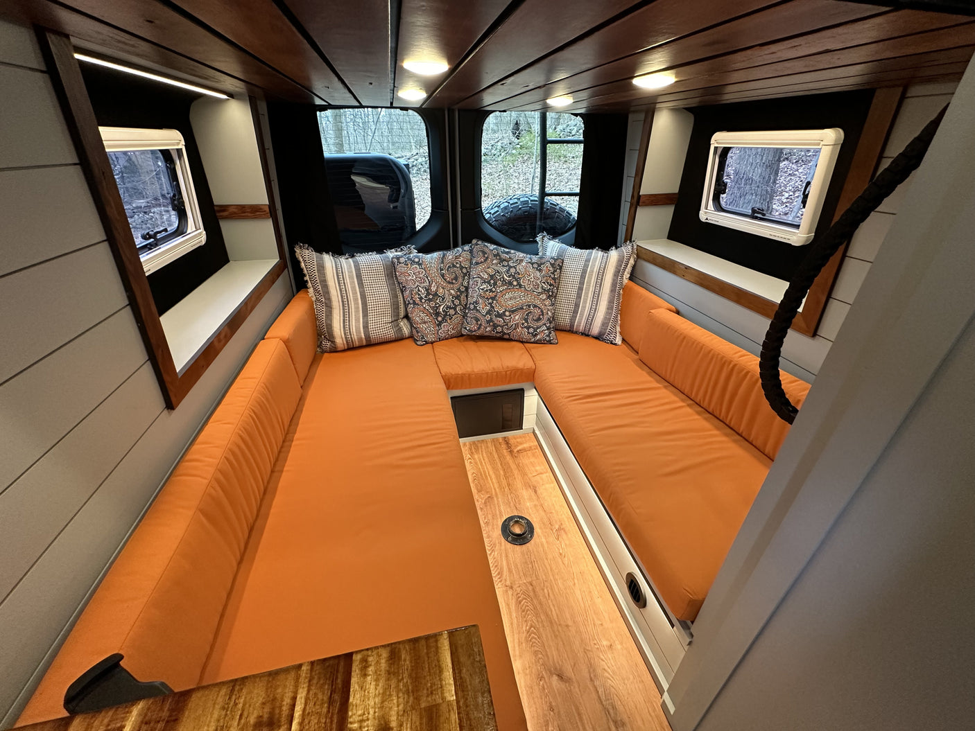 Cozy rv rental interior featuring a spacious U-shaped lounge with vibrant orange cushions, wood accents, and scenic windows.