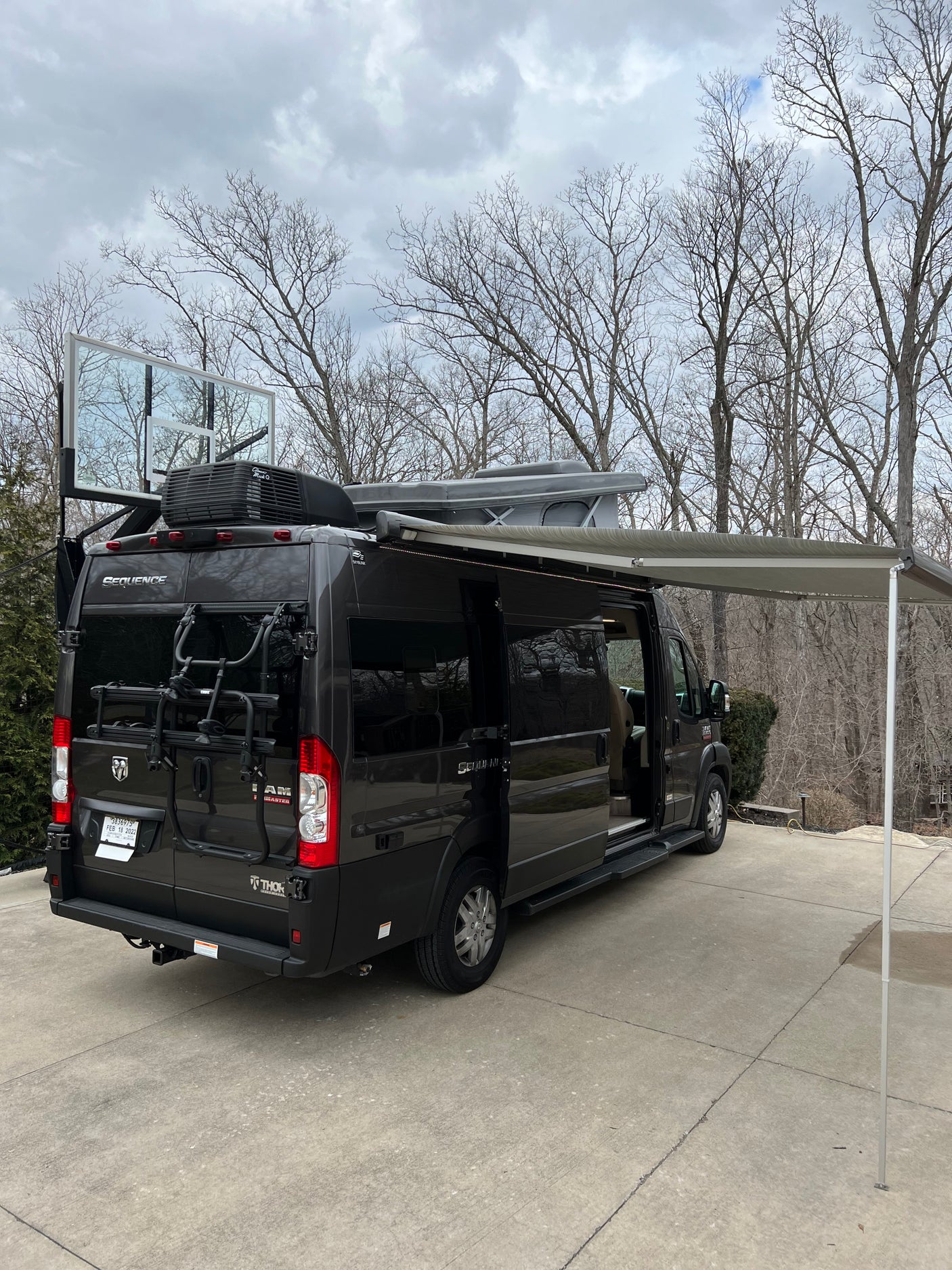 Black rv rental camper van with extended awning, roof-top tent, bike rack, and a unique basketball backboard attachment.