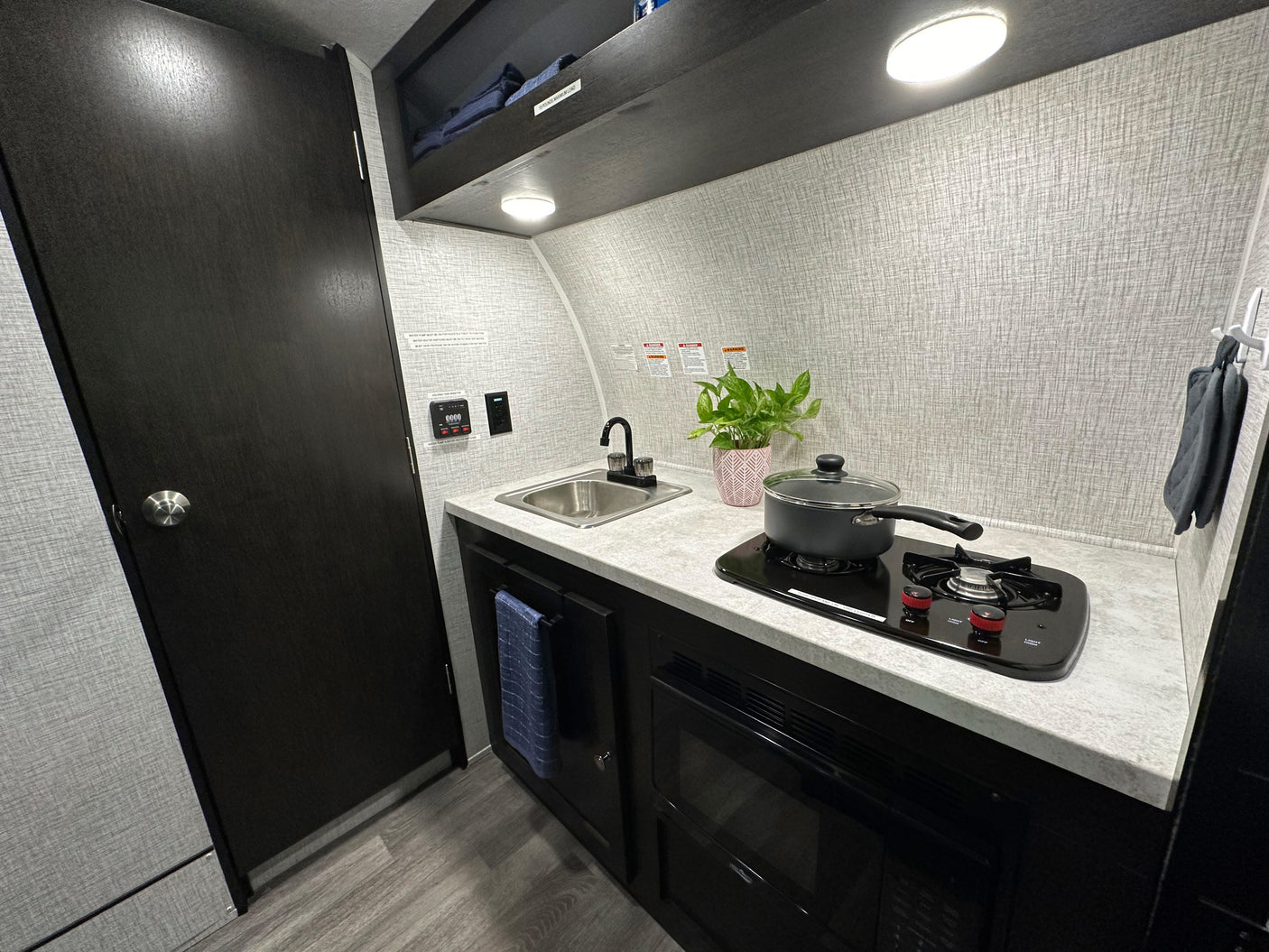 RV rental interior showcasing a compact kitchenette with a sink, two-burner stove, microwave, and overhead storage.
