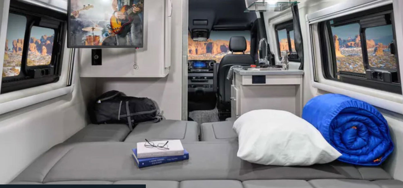 RV rental: Cozy camper van interior features a convertible bed, kitchen, wall-mounted TV, & desert window views.