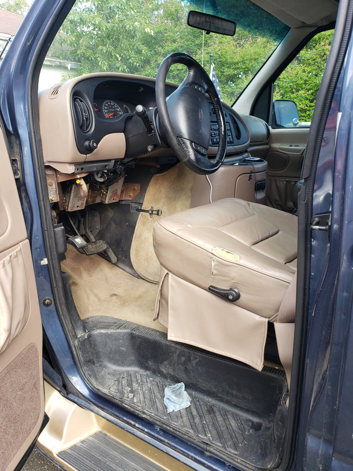 RV rental van interior: driver's seat (torn), exposed dash wiring, steering wheel, and dirty floor mats.