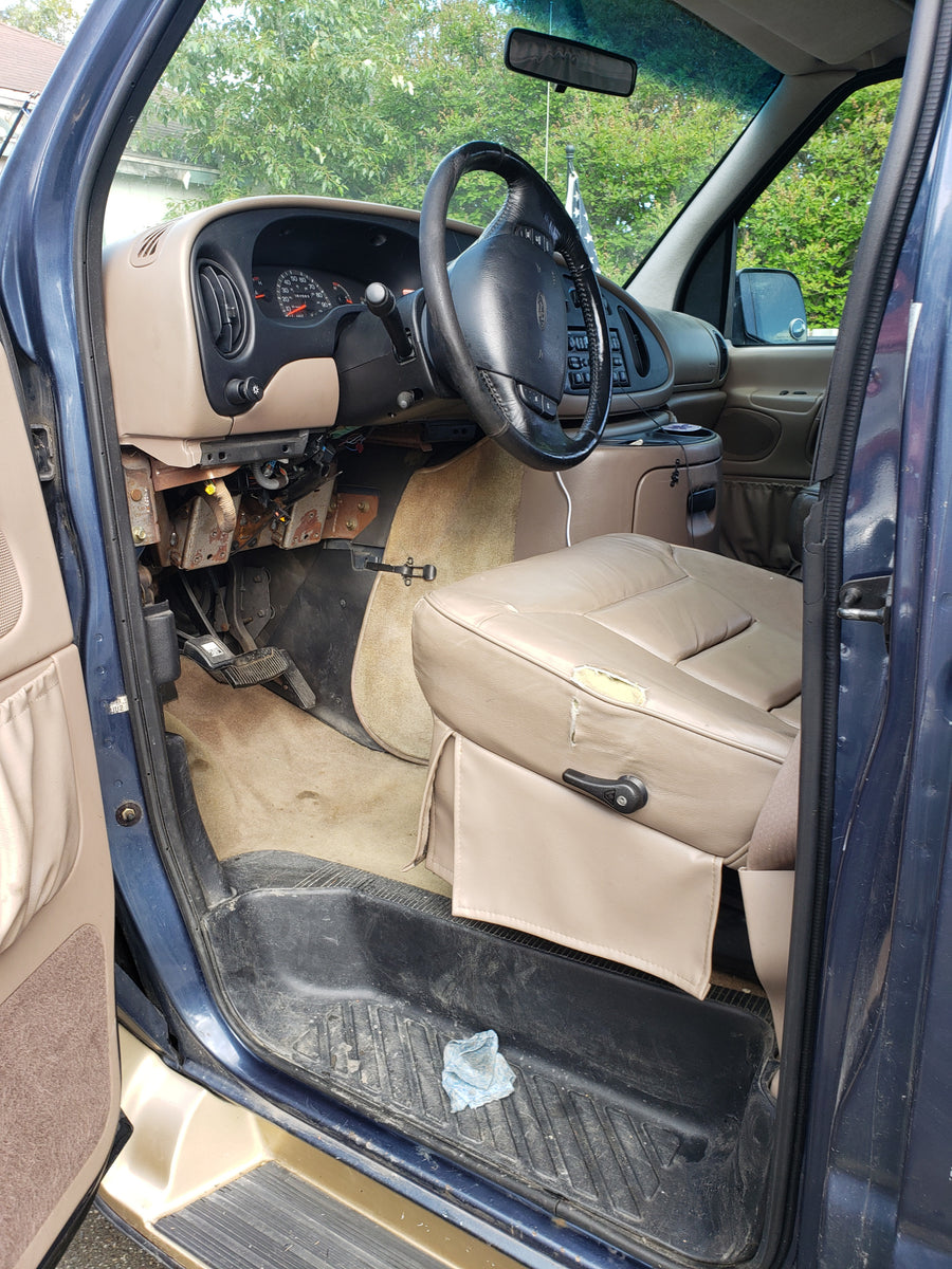 RV rental van interior: driver's seat (torn), exposed dash wiring, steering wheel, and dirty floor mats.