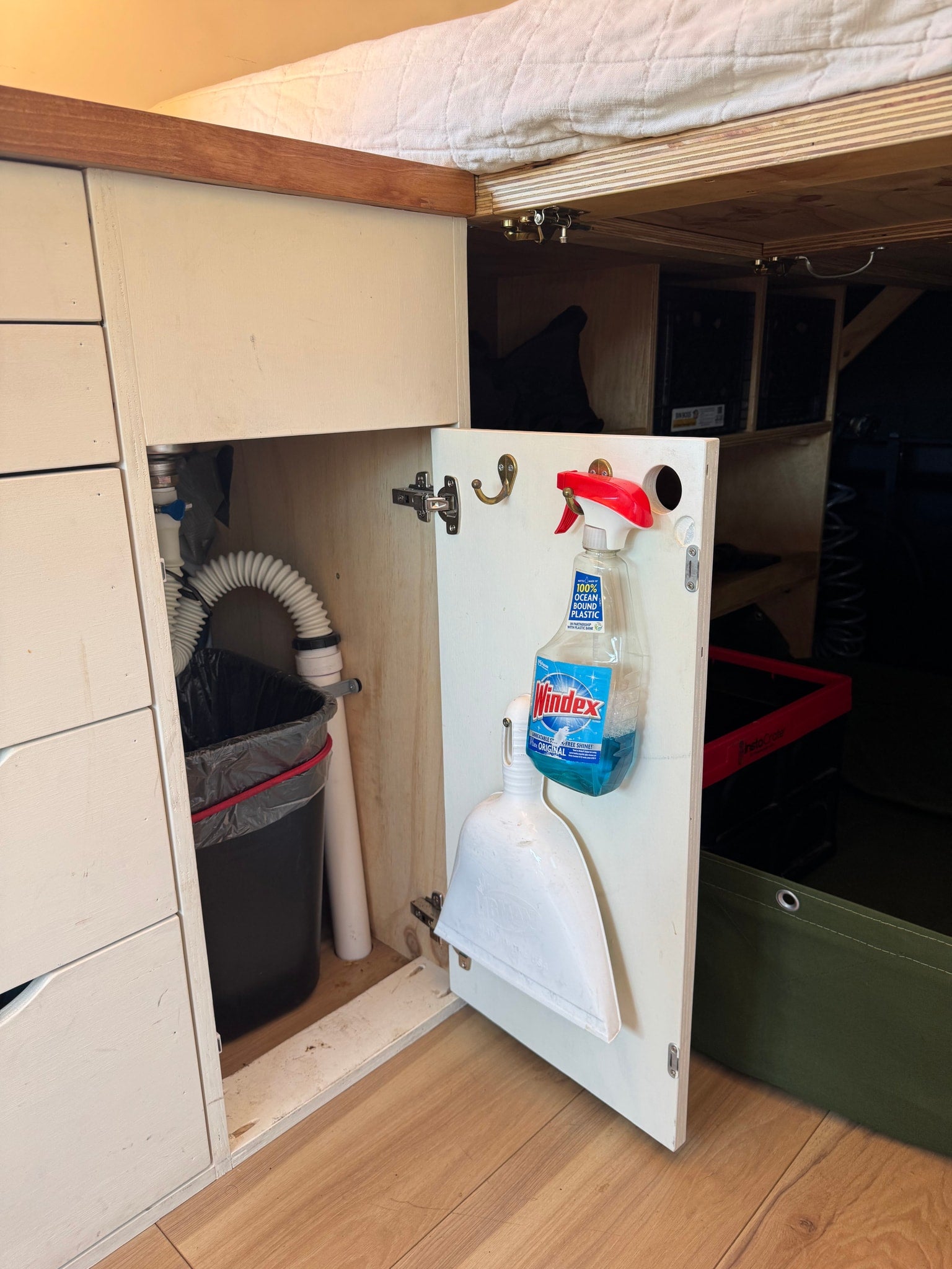 Practical under-bed storage for cleaning supplies (Windex, dustpan) and trash in this RV rental's organized cabinet.