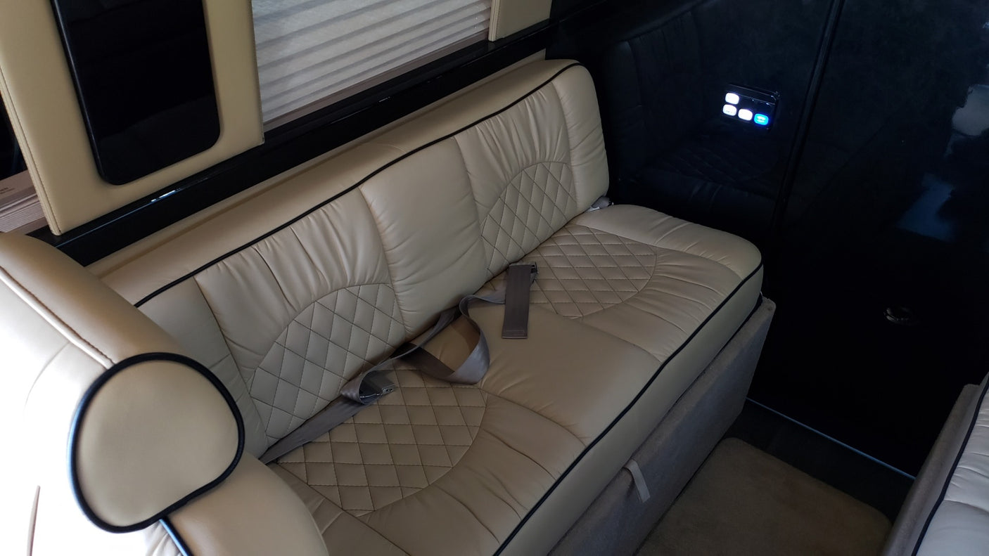RV rental interior: luxurious beige leather bench seating with quilted patterns, seatbelts, and a lit control panel.