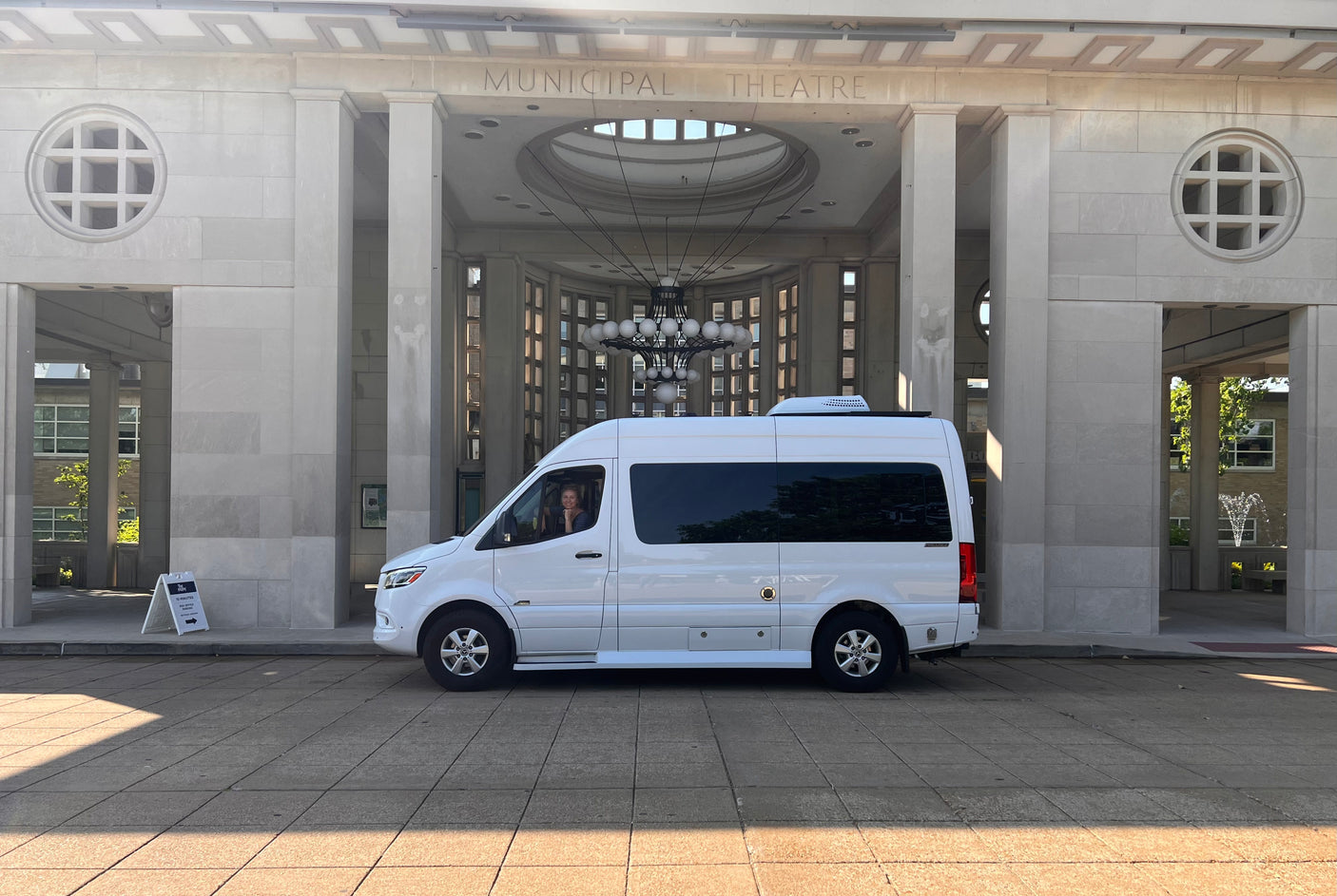 A smiling person in a white RV rental van, parked outside the grand Municipal Theatre.