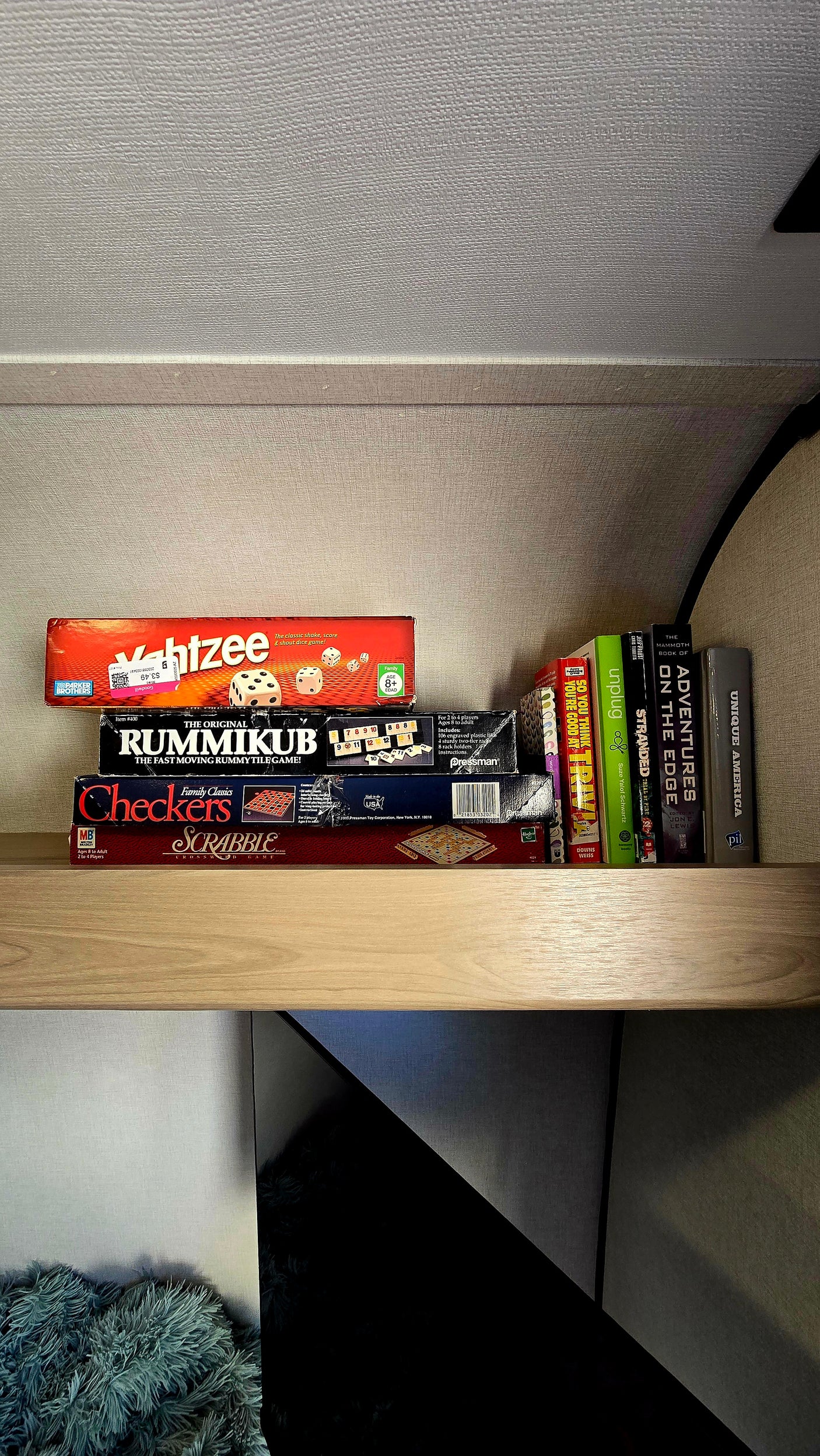 A cozy rv rental shelf is stocked with classic board games like Yahtzee, Rummikub, Scrabble, and various books for entertainment.