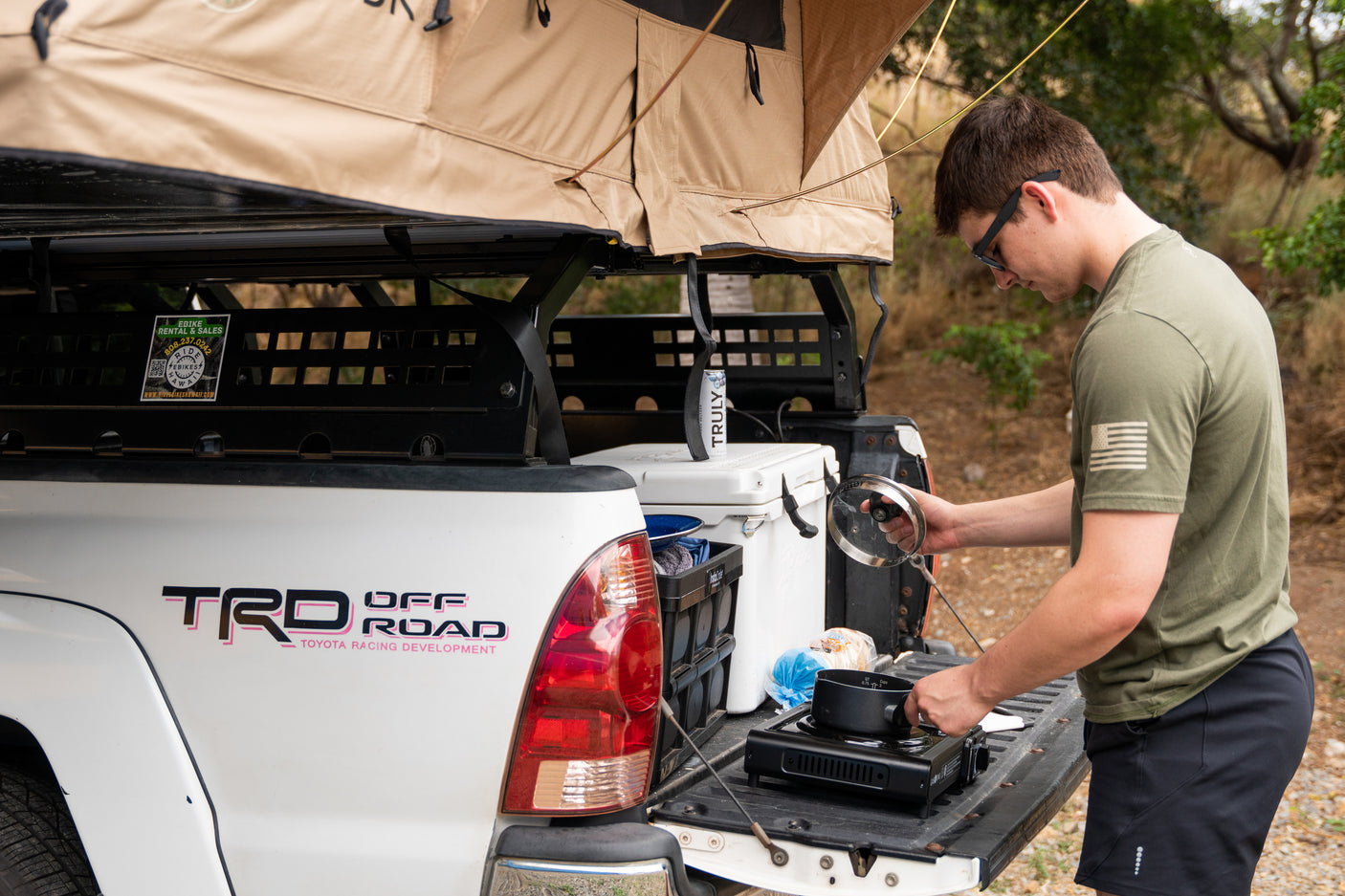 Man preparing food at a truck with a rooftop tent, resembling an RV rental setup for camping trips.