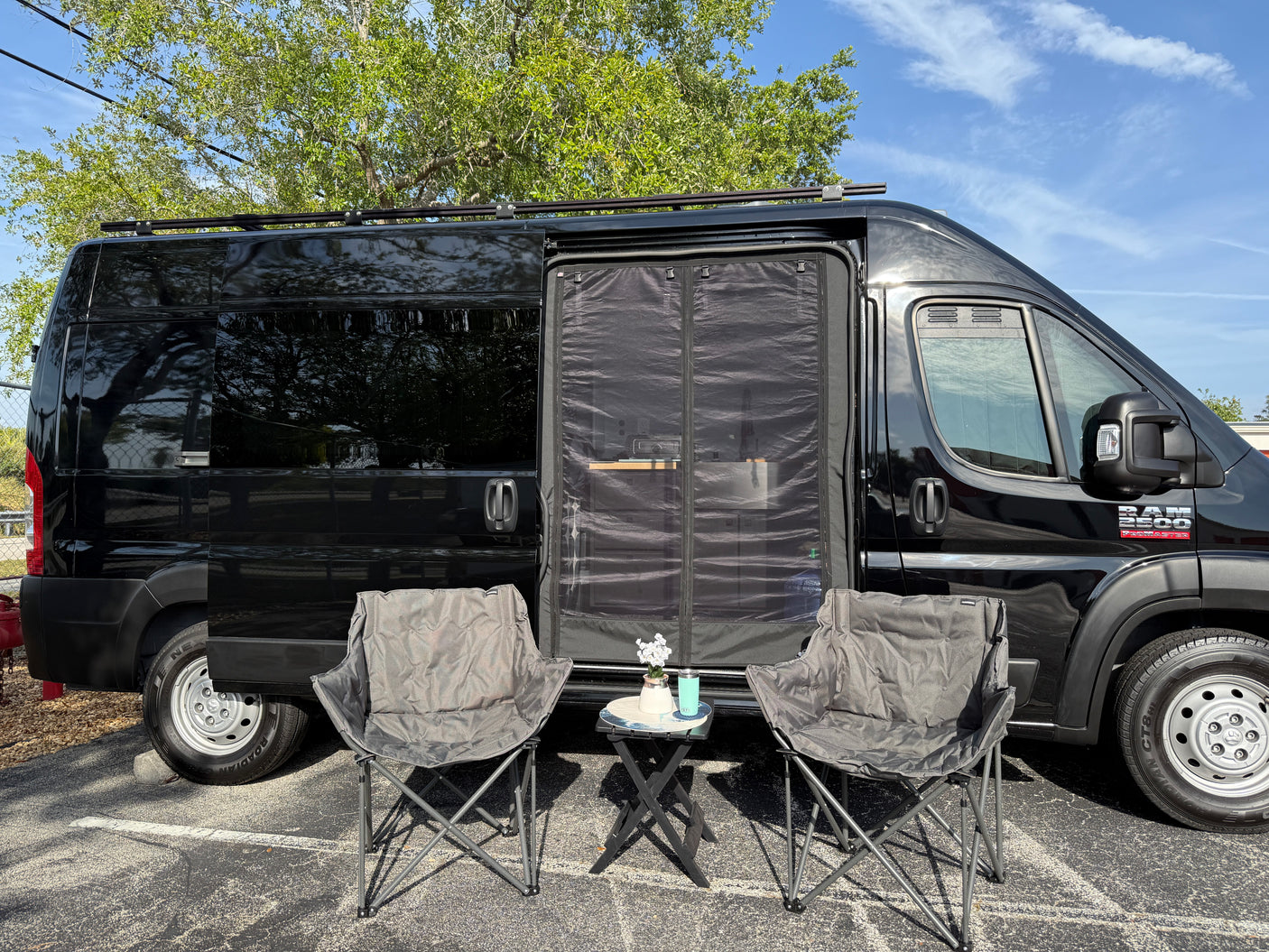 This black Ram ProMaster RV rental is set up for relaxation with a side screen and comfy chairs.
