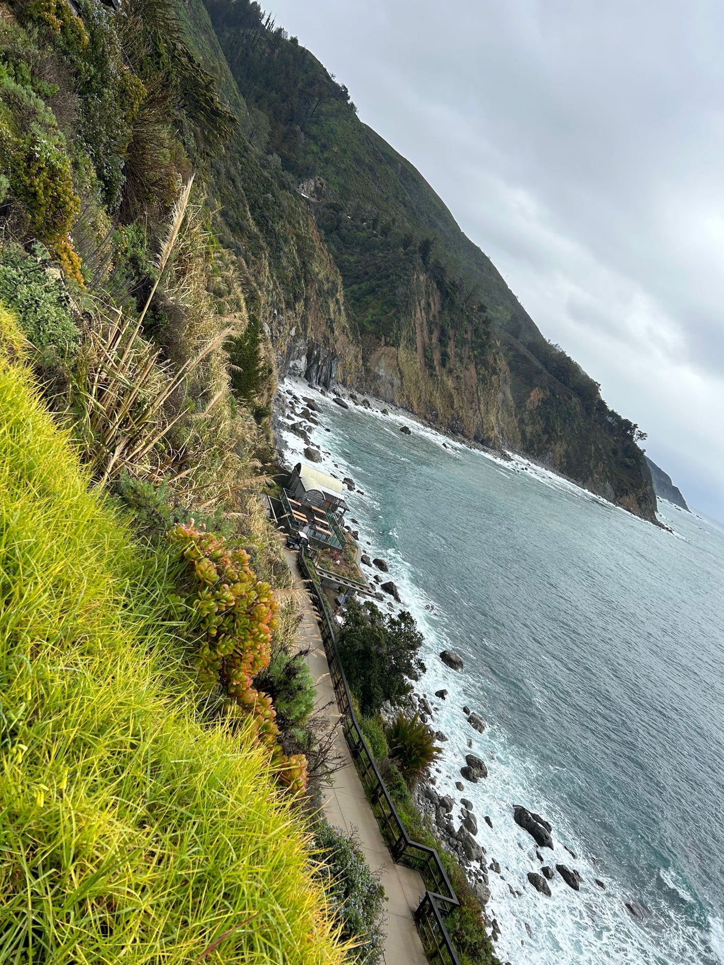 Scenic cliffside path & ocean views, perfect for an RV rental adventure. Discover a charming eatery below.