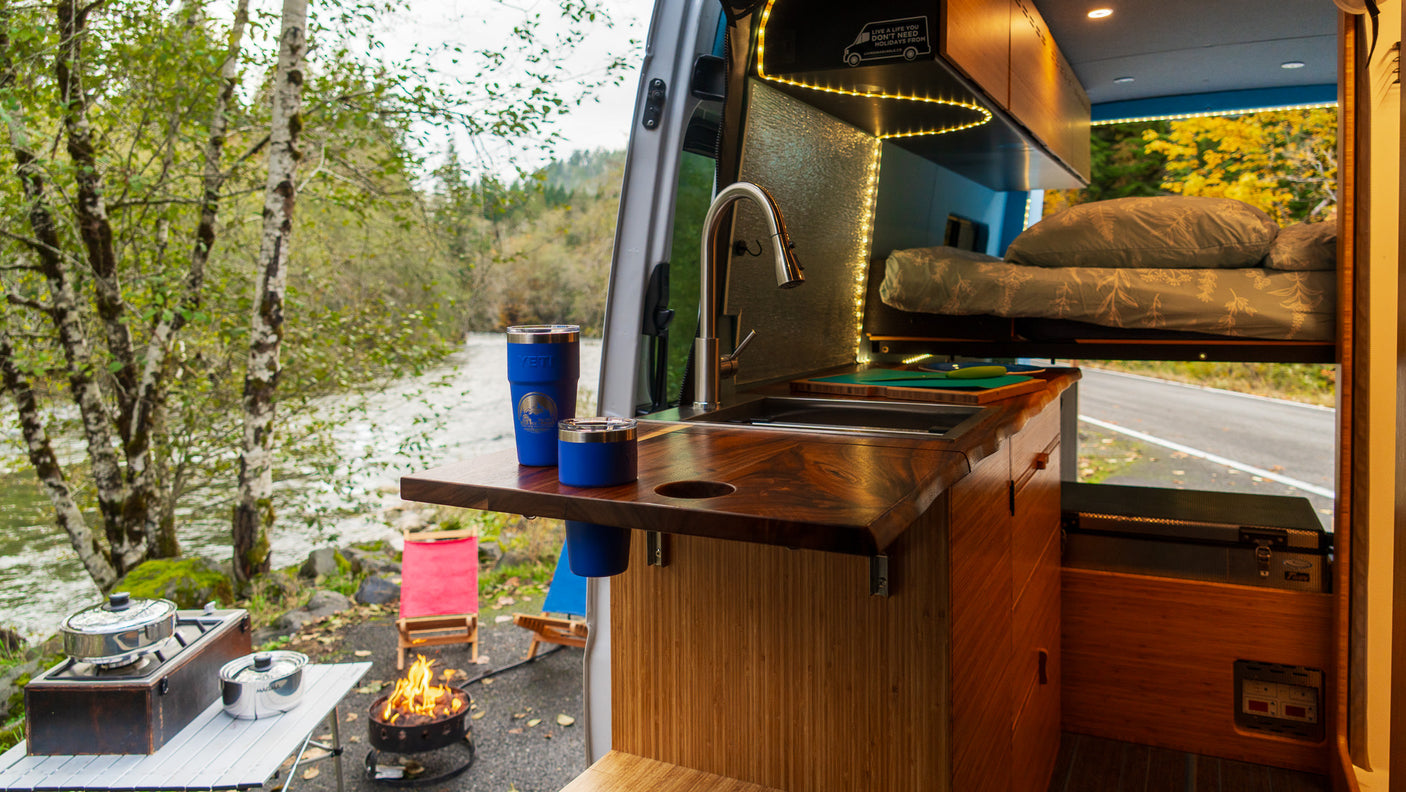 Cozy RV rental interior with kitchen, bed, and river view. Perfect for outdoor cooking by the campfire!